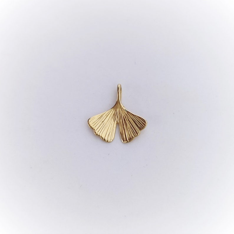 May include: A gold-coloured ginkgo leaf pendant charm. The leaf is detailed with veins and has a smooth, polished finish.
