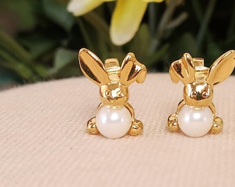 May include: A pair of gold bunny rabbit earrings with a pearl accent. The earrings are small and delicate.