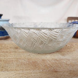 Pode incluir: Tigela de vidro transparente com um padrão texturizado e tecido. A tigela está sobre uma superfície de madeira, com outros objetos de cerâmica no fundo. O design da tigela adiciona um toque de elegância.