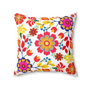 Può includere: Un cuscino bianco con un motivo floreale colorato. I fiori sono rossi, gialli, rosa, blu e verdi. Il cuscino è perfetto per aggiungere un tocco di colore e stile a qualsiasi stanza.