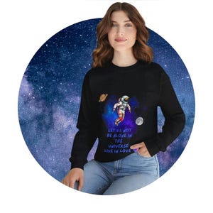 Può includere: Felpa nera con stampa galattica e un astronauta in tuta spaziale. Il testo sulla felpa recita "Let us not be alone in the universe, live in love."