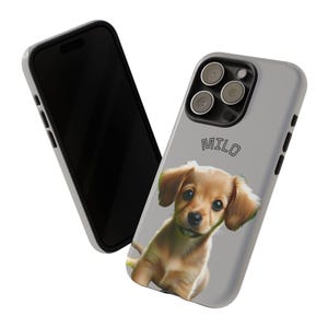 Peut inclure: Coque de téléphone gris clair avec un chiot marron et le nom "MILO". Un smartphone noir est à côté de la coque.