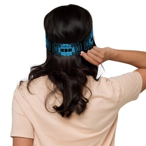 Puede incluir: Una diadema azul y negra con un patrón geométrico. La diadema se lleva en la cabeza de una persona.