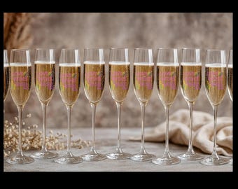May include: A row of champagne flutes filled with bubbly liquid. Each glass has a pink and yellow design that reads "Have a fabulous day". The glasses are on a gray surface with a neutral background.