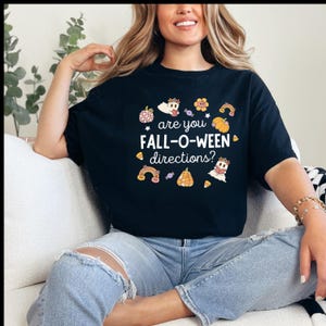 Könnte beinhalten: Schwarzes T-Shirt mit dem Text "are you FALL-O-WEEN directions?" und Halloween-Grafiken. Die Grafiken umfassen Kürbisse, Geister, Regenbogen und Süßigkeiten. Das T-Shirt wird von einer Person getragen.