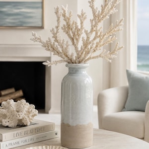 May include: A tall, cylindrical ceramic vase with a glossy light blue upper section and a matte, textured beige base. The vase contains a large, branching off-white coral-like decorative stem, creating a tall, airy arrangement with a natural aesthetic.