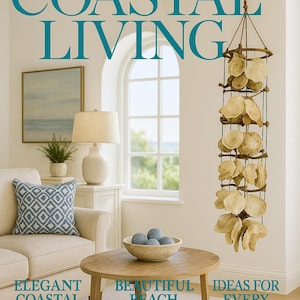 May include: A living room scene with a coastal theme. A hanging shell mobile is suspended from the ceiling. A round wooden coffee table holds a bowl with blue spheres. The text "COASTAL LIVING" is at the top of the image.