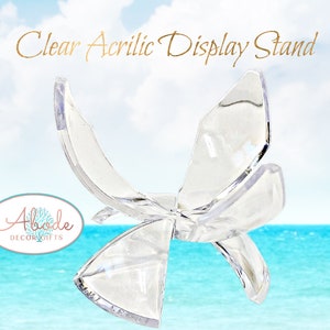 May include: Clear acrylic display stand shaped like a butterfly. The stand is made of clear acrylic and has a simple design. It is perfect for displaying small items, such as jewelry, figurines, or other collectibles.