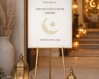 May include: A gold easel displays a sign with Arabic calligraphy and the text "Welcome to The Mustafa's Iftar Dinner, March 10th, 2026." Decorative gold lanterns with lit candles and white flowers flank the sign, creating an elegant ambiance.