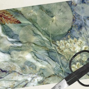 May include: A digitally created marble-like background with a botanical design. The color palette includes shades of green, blue, and gold. Delicate, fan-shaped leaves and floral elements are scattered across the surface. A pair of scissors is in the bottom right corner.