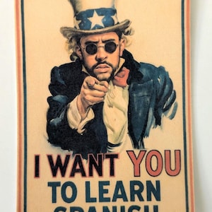 May include: A rectangular print featuring a man in a top hat and sunglasses, pointing at the viewer. The text reads "I WANT YOU TO LEARN SPANISH" in red and black. The image has a vintage poster style.