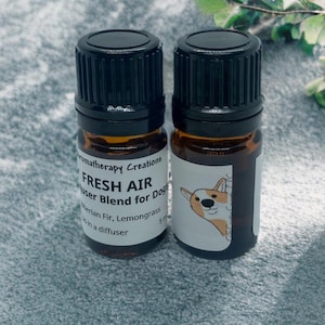 Peut inclure: Deux petits flacons en verre brun avec des bouchons noirs, étiquetés "FRESH AIR diffuser Blend for Dogs Siberian Fir, Lemongrass 5 ml". L'étiquette présente également un chien de dessin animé.