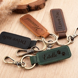 May include: Leather keychains in black, brown, and green, each with a metal clasp and ring. The keychains are engraved with the words "Drive safe", "Hannah", "I Love You", and "Estelle" with paw prints.