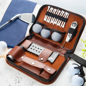 May include: A brown leather golf kit with a zipper, containing golf balls, tees, a divot repair tool, and a multi-tool. A blue towel and a golf club are also visible.