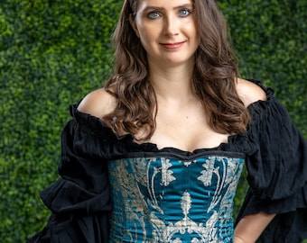 May include: A woman wearing a blue and silver brocade corset with a black off-the-shoulder top and a black and blue ruffled skirt.