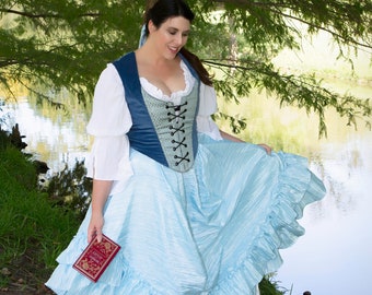 May include: A woman wearing a blue and green corset with a white blouse and a light blue ruffled skirt. She is holding a small red book in her hand. The skirt has multiple layers of ruffles and is very full.