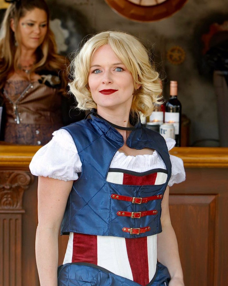 May include: A woman wearing a blue and red corset with a white top and a blue vest. The corset has a red, white, and blue pattern and is decorated with buckles.