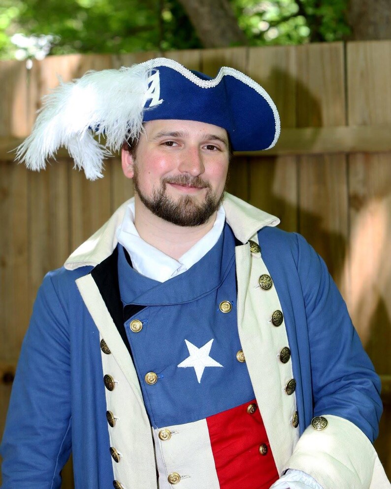 May include: A man wearing a blue and white colonial-style jacket with a white feather hat. The jacket has a star on the chest and a red, white and blue stripe on the bottom.
