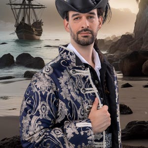 May include: A man wearing a black leather hat with a feather and a navy blue and silver brocade coat. The coat has ornate silver buttons and trim. A pirate ship is in the background, suggesting a costume or historical theme.