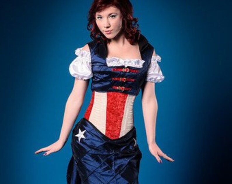 May include: A red, white, and blue corset with a star on the skirt. The corset has a busk closure and is made of a satin-like fabric.