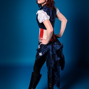 May include: A woman wearing a blue and red corset with white stars and a blue skirt with white stars. She is wearing black tights and black boots with buckles. The background is blue.
