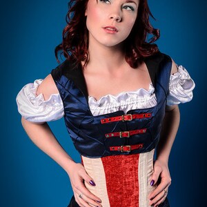 May include: A woman wearing a blue and red corset with a white ruffle collar and white sleeves. The corset has a quilted design and is fastened with buckles. The woman is wearing a blue skirt with a white star.
