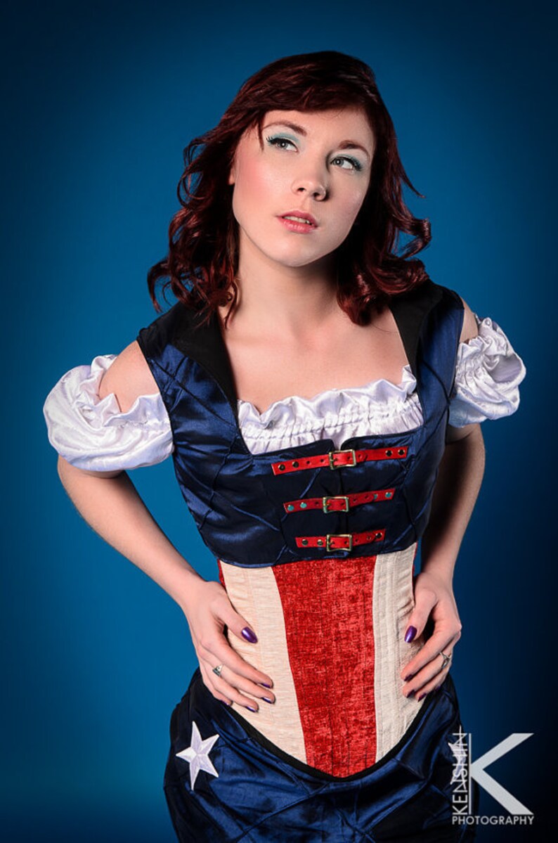 May include: A woman wearing a blue and red corset with a white ruffle collar and white sleeves. The corset has a quilted design and is fastened with buckles. The woman is wearing a blue skirt with a white star.