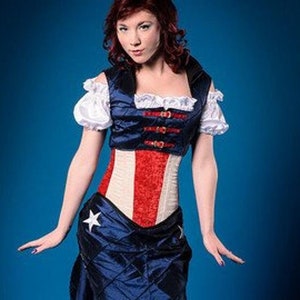 Puede incluir: Una mujer con un cors&eacute; rojo, blanco y azul, una falda azul marino y una blusa blanca con ribetes rojos y azules. El cors&eacute; tiene una estrella en la parte delantera y la falda tiene un patr&oacute;n acolchado.