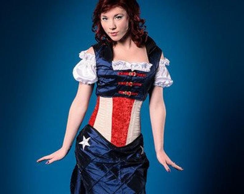 Puede incluir: Una mujer con un cors&eacute; rojo, blanco y azul, una falda azul marino y una blusa blanca con ribetes rojos y azules. El cors&eacute; tiene una estrella en la parte delantera y la falda tiene un patr&oacute;n acolchado.