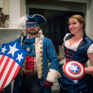 May include: Two people dressed as Captain America, one in a blue and white costume with a red, white and blue shield, and the other in a blue and white dress with a red, white and blue shield.