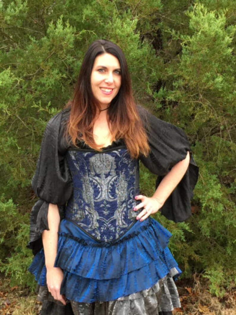 May include: A woman wearing a blue and silver corset with a black top and a blue ruffled skirt.