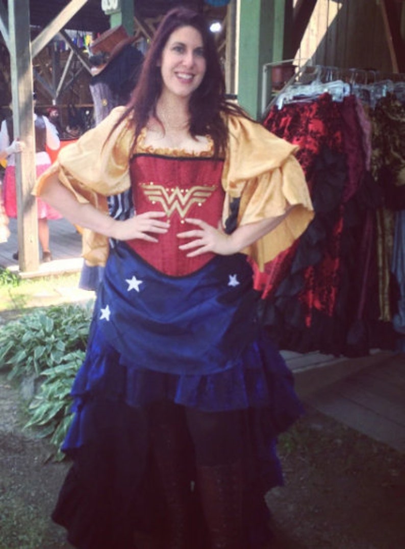 May include: A woman wearing a red and gold corset with a Wonder Woman logo, a blue and white skirt with stars, and a gold shawl.