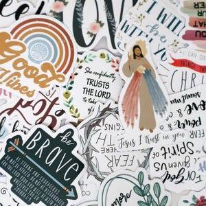 Puede incluir: Una colección de pegatinas variadas con citas inspiradoras e imágenes religiosas. Los diseños incluyen un arcoíris, detalles florales y las palabras "Good Vibes", "Be Brave" y "She confidently TRUSTS THE LORD". Las pegatinas son blancas con varios colores.