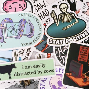 Puede incluir: Una colecci&oacute;n de pegatinas coloridas con varios dise&ntilde;os y texto. Una pegatina presenta un esqueleto haciendo una se&ntilde;al de pulgar hacia arriba con las palabras "Stay Positive". Otra dice "I am easily distracted by cows". Otras pegatinas tienen frases e ilustraciones.