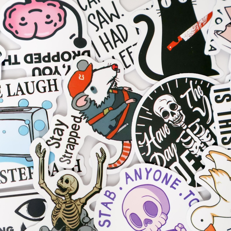 Puede incluir: Una colecci&oacute;n de varias pegatinas con ilustraciones de dibujos animados y texto. Las pegatinas presentan una rata con un atuendo de construcci&oacute;n, un gato negro con un cuchillo, un esqueleto y un cerebro. El texto incluye "SAW. I HAD EF", "Stay Strapped" y "Have a Day".