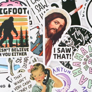 Puede incluir: Una colecci&oacute;n de pegatinas coloridas con varios dise&ntilde;os y texto. Una pegatina presenta una silueta de Bigfoot con el texto "Doesn't Believe in You Either". Otras pegatinas incluyen un retrato de Jes&uacute;s, una calavera y una imagen vintage de una ni&ntilde;a por tel&eacute;fono.