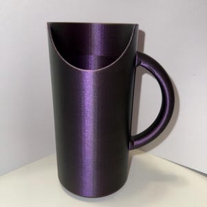 May include: A dark purple ceramic mug with a unique handle design. The mug has a smooth, glossy finish.