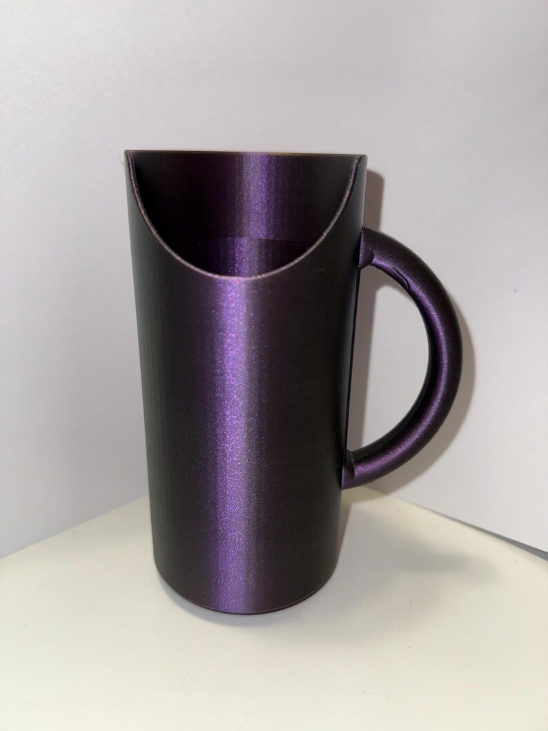 May include: A dark purple ceramic mug with a unique handle design. The mug has a smooth, glossy finish.