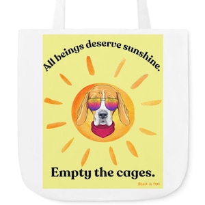 Könnte beinhalten: Eine weiße Einkaufstasche mit einer gelben Sonne und einem Beagle, der eine Sonnenbrille trägt. Der Text auf der Tasche lautet "Alle Wesen verdienen Sonnenschein. Leere die Käfige. Gnade ist frei."