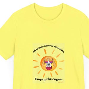 May include: A bright yellow t-shirt featuring a graphic of a beagle wearing sunglasses and a red bandana, set against a sunburst design. The text "All beings deserve sunshine" and "Empty the cages" are also displayed.