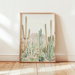 May include: A framed print of a watercolor painting of a desert landscape with various cacti in shades of green and brown. The cacti are arranged in a cluster, with a mountain range in the background.