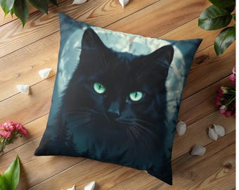 May include: Square decorative pillow featuring a black cat with glowing green eyes against a backdrop of a full moon and a dark forest. The cat's fur is detailed, and the pillow has a soft, inviting appearance. The pillow is a home decor item.