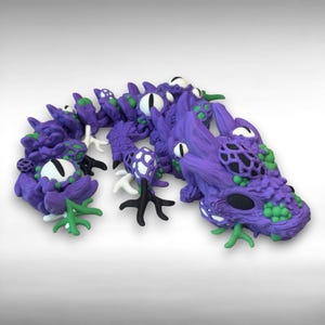 May include: A purple dragon sculpture with white eyes, green accents, and black details. The dragon has a textured body and is posed in a curved shape. The sculpture is made of a solid material.