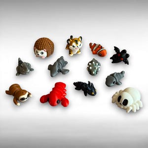May include: A collection of small, colorful animal figurines. The assortment includes a hedgehog, tiger, clownfish, shark, sloth, lobster, and spider. Each figurine is uniquely designed with detailed features and vibrant colors.