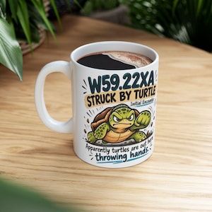 May include: A white ceramic mug featuring a graphic of an angry green turtle with a brown shell. The text reads W59.22XA STRUCK BY TURTLE Initial Encounter Apparently turtles are out here throwing hands. The mug has a handle and a dark liquid inside.