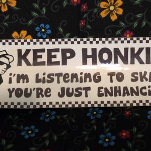 Può includere: Adesivo bianco per paraurti con testo nero: "KEEP HONKING! I'm LISTENING TO SKA, and YOU'RE JUST ENHANCING IT!" Una figura di cartone animato in bianco e nero in giacca e occhiali da sole è a sinistra. L'adesivo ha un bordo a scacchi in bianco e nero.