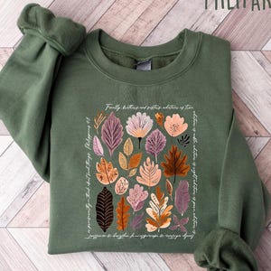 May include: Military green sweatshirt featuring a floral design with leaves and flowers in shades of orange, pink, and purple. The text "Finally brothers and sisters, whatever is true..." is printed on the front. The sweatshirt has long sleeves.