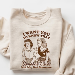 May include: A beige sweatshirt with a brown graphic print of two women. The text on the graphic reads "I want you to know that someone cares. Not me, but someone."