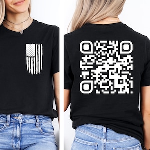 May include: Black t-shirt with a white American flag design on the front and a white QR code on the back. The shirt is being modeled by a person wearing blue jeans.
