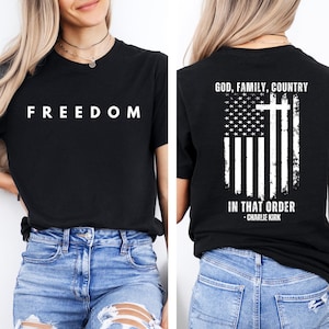 Peut inclure: T-shirt noir avec le mot "FREEDOM" en lettres blanches sur le devant. Le dos du t-shirt pr&eacute;sente un motif de drapeau am&eacute;ricain vieilli avec une croix et le texte "GOD, FAMILY, COUNTRY IN THAT ORDER - CHARLIE KIRK."